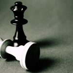 A low-angle shot of a chess game in progress, with the black king tipped over on the board.