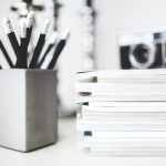 A stack of colorful spiral notebooks with a handful of sharpened pencils resting on top