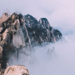 Jagged mountain peaks piercing through a thick layer of white mist and clouds