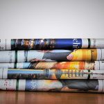 A stack of four rolled up newspapers on a wooden surface.