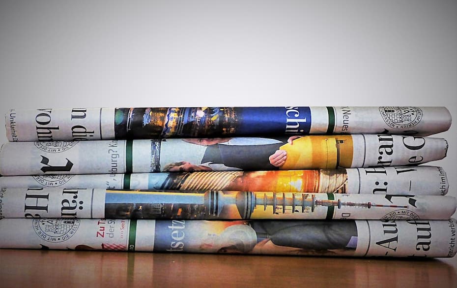 A stack of four rolled up newspapers on a wooden surface.